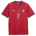 Portugal Home Football Shirt 2026 Puma crimson bright red showing tonal red horizontal wave ripple jacquard texture pattern across full shirt FPF red cross crest blue Quinas shield white Puma leaping cat logo No.7 white on chest teal emerald green V-neck collar 4-pointed star detail teal cuff trim Puma DRYCELL RE:FIBRE badge front flat lay view on white background