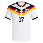 Germany Home Football Shirt 2026 Adidas white showing bold black red gold yellow German tricolor diagonal chevron V-shaped crossing stripe graphic on chest DFB black eagle crest 4 gold stars white Adidas 3-bar logo No.17 black on chest black V-neck collar red inner accent black Adidas 3-stripe shoulders black red cuff trim front view on white background