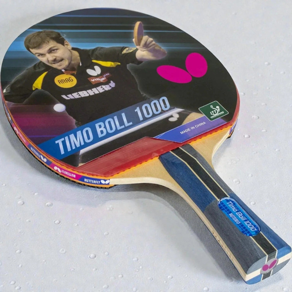Butterfly Timo Boll 1000 Table Tennis Racket front view showing Timo Boll photo label red rubber face blue striped handle and pink Butterfly logo - product front view